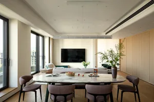 Open living area with a white couch, two chairs, a dining table, potted plants, and a vase, set against a neutral background