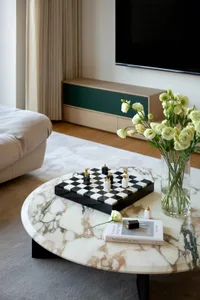 A cozy living room with a black coffee table, chess set, vases of flowers, and scattered books, creating a warm and inviting atmosphere