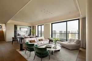 Open living area with a white couch, chairs, dining table, vases, and potted plants, surrounded by natural light from a window