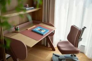 A calm and organized office space with a pink desk, two chairs, and a book, set against a neutral-toned background