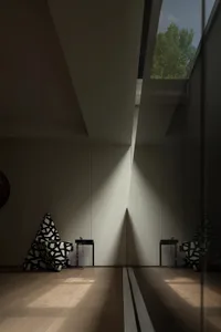 A modern minimalist living area with a large white wall reflecting sunlight, two chairs, and a dining table
