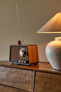 A vintage radio sits on a wooden table in a cozy living area with a small lamp nearby
