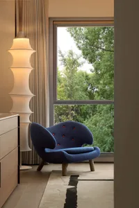 Cozy living space with a blue armchair, two lamps, and a large window providing natural light