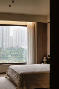Cozy bedroom with a large window offering a city view, a bed near the window, and two vases on either side