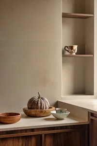A kitchen countertop with three bowls, two cups, two spoons, and a pumpkin, set against a neutral background