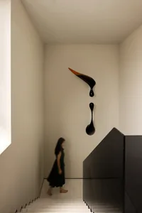 A woman in a green dress walks down a well-lit hallway with two sculptures on display, one with dripping black paint