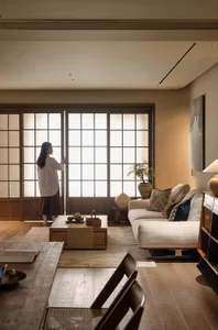 Cozy living space with a white couch, chairs, dining table, and a potted plant, lit by natural light through open doors