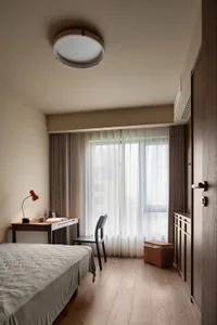 A bedroom with a bed and desk, natural light from two windows, and a lamp, set against a clean and bright white wall background