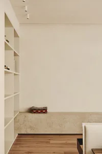 Empty minimalist living area with white walls and a concrete floor, featuring bookshelves and a bench
