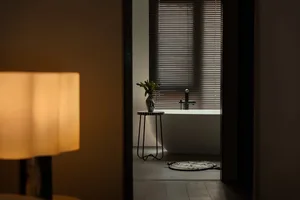 Dimly lit bathroom with a bathtub, black faucet, and vases on a table in front of the tub