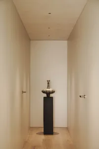 Empty hallway with white walls, a black metal vase on a pedestal, and a minimalist aesthetic