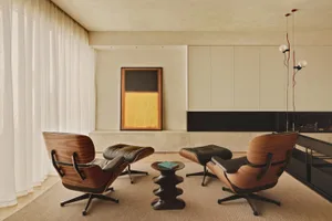 A cozy living area with two black leather chairs, a carpeted floor, and two couches, a dining table, and a book, surrounded by warm wood accents