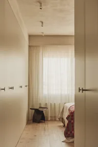 A serene bedroom with two beds, a chair, and a white wall, with a window letting in natural light