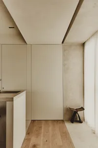 Empty modern kitchen with white cabinets, a sink, and a chair, set against a concrete wall background