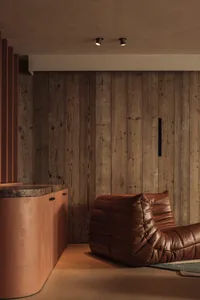 Dimly lit living space with a brown leather chair, wooden wall, and wood paneling
