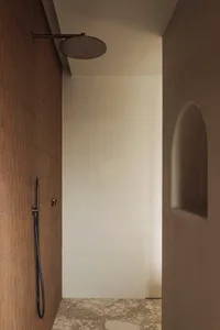 Bathroom with a brown tile wall, a shower stall, and a black hose for water supply