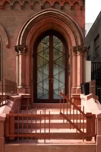 A historic building with a red brick facade, a large archway entrance, and a stained glass window above the doorway, giving it a solid and durable appearance