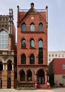 A historic building with a mix of Gothic elements, red brick walls, and varied window sizes and shapes, giving it a sense of depth and complexity