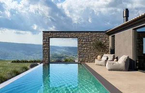 Outdoor living area with a large pool surrounded by stone walls, featuring two leather couches for relaxation