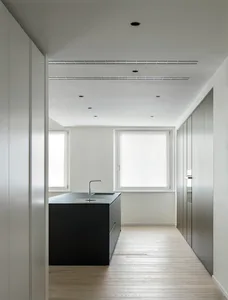 Modern kitchen with white cabinets, black countertops, and natural light from two windows, featuring a dining table and kitchen island