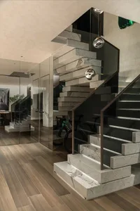 A well-maintained interior staircase with a marble stairwell, glass walls, wooden stairs, and a metal railing, featuring bicycles and a potted plant