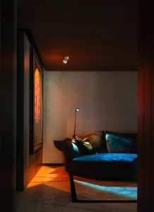Cozy living space with a black couch, two chairs, and a small table, surrounded by artwork and suggesting a comfortable atmosphere