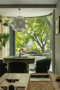 A cozy dining area with a wooden table and green cushioned chairs, natural light, and a potted plant near the window