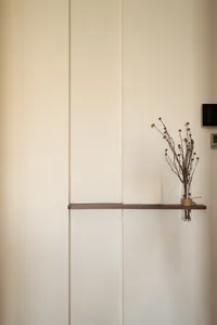 A calm interior space with a white wall, wooden shelf, and vases with flowers, creating a peaceful atmosphere