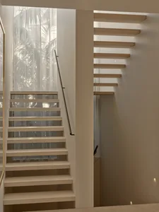 A well-lit interior staircase with two sets of stairs, one on each side, in a residential home with a white color scheme and wooden stairs