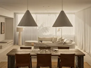 Open modern living area with a white couch, chairs, and dining table, surrounded by natural light and clean lines