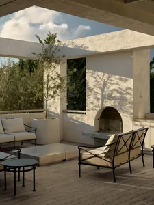 An inviting outdoor living area with a white fireplace, large window, and comfortable seating options, featuring a potted plant and a relaxed atmosphere