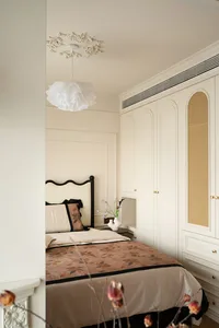Cozy bedroom with a large bed, nightstands, a dresser, and a chair, surrounded by white walls and a brown blanket