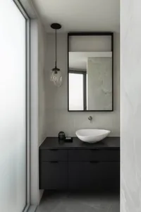 A small bathroom with a white sink, mirror, and window, featuring two bottles on the countertop and a clean, organized atmosphere