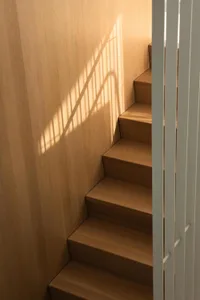 A wooden staircase with brown tones, well-lit and inviting, with a shadow on the adjacent wall