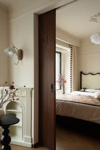 A calm bedroom with a wooden door, a large bed, two vases, and a potted plant, with natural light from the window