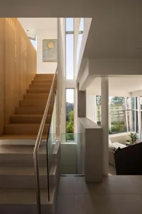 Modern living space with a staircase leading to a second floor, featuring a white color scheme, wooden stairs, and a glass railing