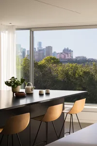 Modern kitchen with wooden chairs, a dining table, and potted plants, featuring a large window with a city view