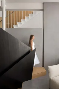 A woman in a white dress walks down a staircase with a black railing in a well-designed interior space