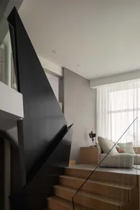 Open modern living space with a black spiral staircase, two couches, a chair, and decorative vase, featuring a stylish and functional design