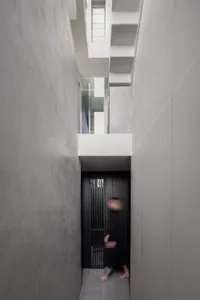 A person walks down a narrow hotel hallway with dark walls and two doors on either side