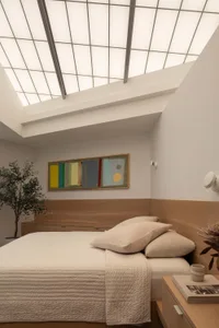 A cozy bedroom with a wooden headboard, white bedding, and potted plants, featuring a relaxing atmosphere