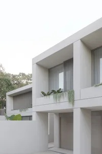 Two white buildings with large windows, one with a balcony and plants, the other with ivy-covered wall, in a calm and serene atmosphere