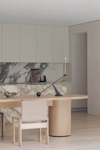 Warm and inviting modern kitchen with marble countertops, a wooden dining table, and white cabinets
