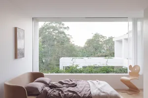 A cozy bedroom with a comfortable bed near a large window offering a view of surrounding greenery, accompanied by two chairs and a relaxing atmosphere