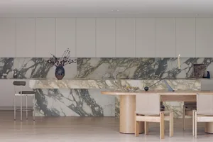 Modern kitchen with marble countertops, a wooden table, and a large island, featuring clean and organized space with a focus on functionality and aesthetics