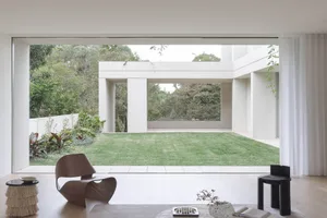 Open modern living area with a glass door leading to a backyard patio, featuring a cozy seating arrangement, dining table, and potted plant, with plenty of natural light through large windows
