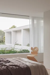A bright and inviting bedroom with a large window, two chairs, a couch, and greenery outside