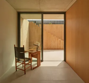 A modern living and dining space with two chairs, a small table, and cement walls, giving a functional and industrial feel