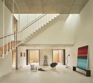 Bright and inviting open living area with a white staircase, minimalist design, two chairs, a couch, and natural light from windows