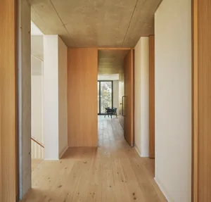 Open living area with hardwood floors, white walls, and natural light from windows, featuring a chair and two doors